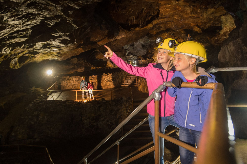 Zwei Mädchen mit gelben Sicherheitshelmen betrachten das Bergwerk, im Hintergrund die Eltern