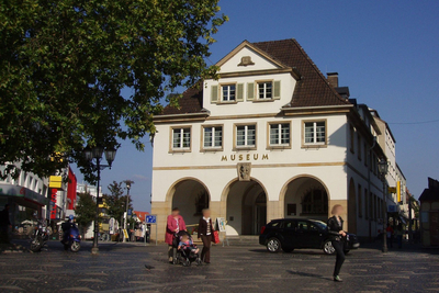 Marktplatz mit Passanten und Haupteingang des Museums mit markanten Arkadenbögen
