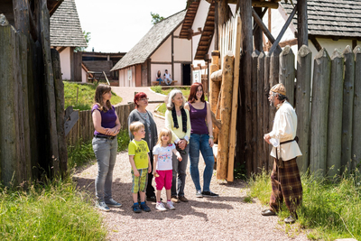 Gästeführer in keltischen Gewandung führt eine kleine Gruppe von Besuchern mit Kindern