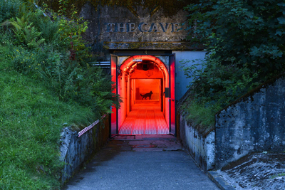 Außenansicht des rotausgeleuchteten Eingang zum Bunker mit Aufschrift 'THE CAVE' darüber
