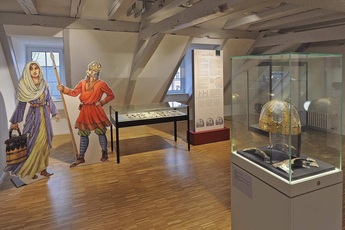Ausstellungsraum mit Vitrine des vergoldeten Helms von Pfeffingen und lebensgroßer Figur des Helmträgers mit einer Frau