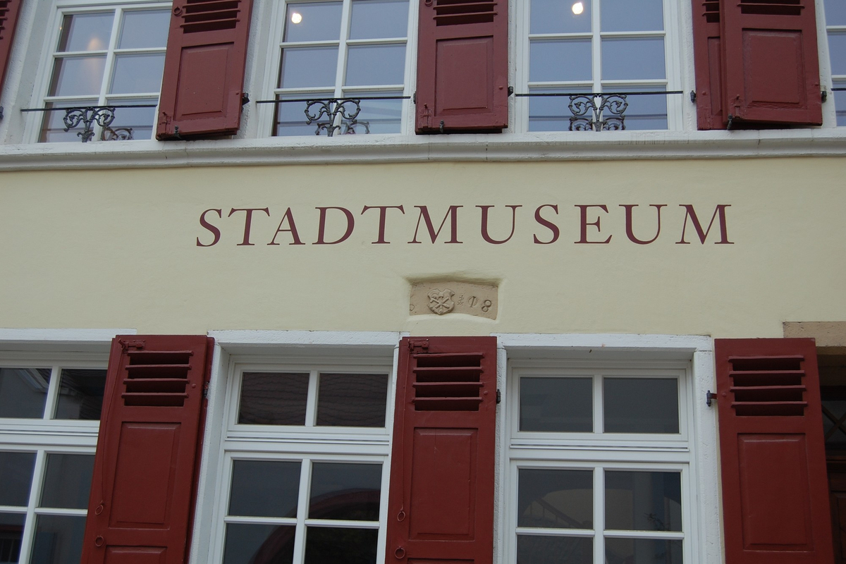 Detail der Front des Museumsgebäudes mit Schriftzug „Stadtmuseum“ und Sprossenfenstern mit roten Fensterläden